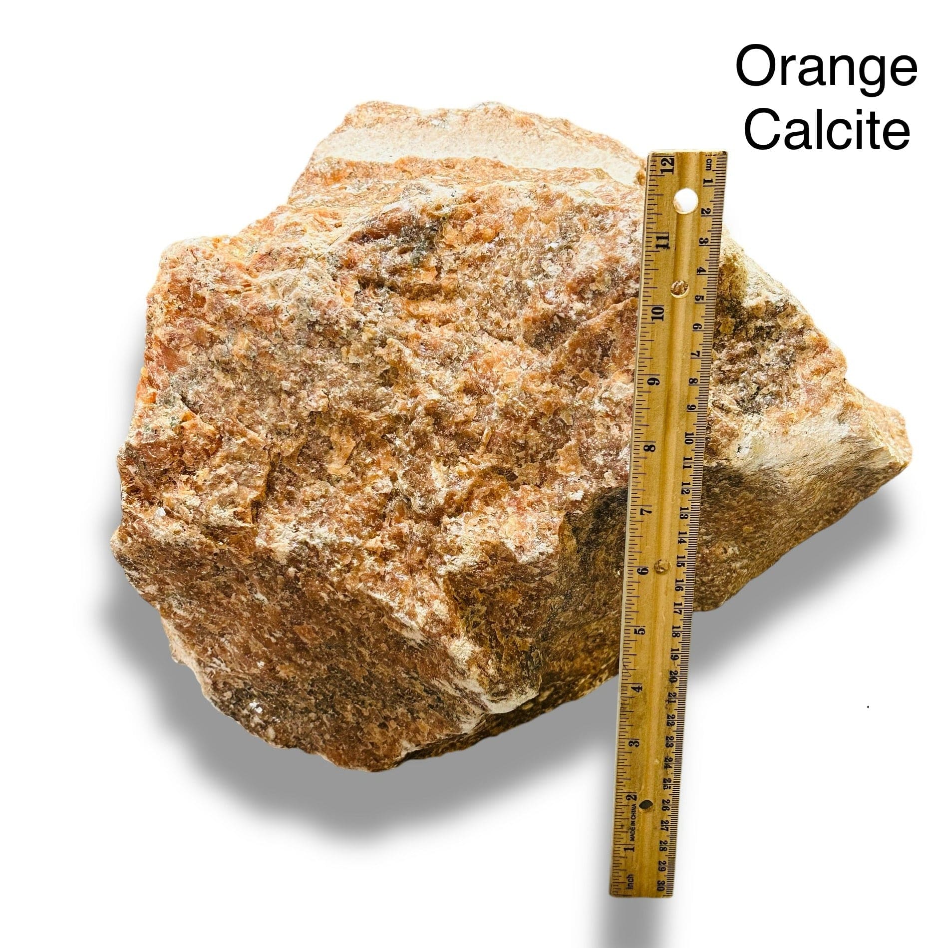 large orange calcite rough stone crystal next to a ruler for size reference 