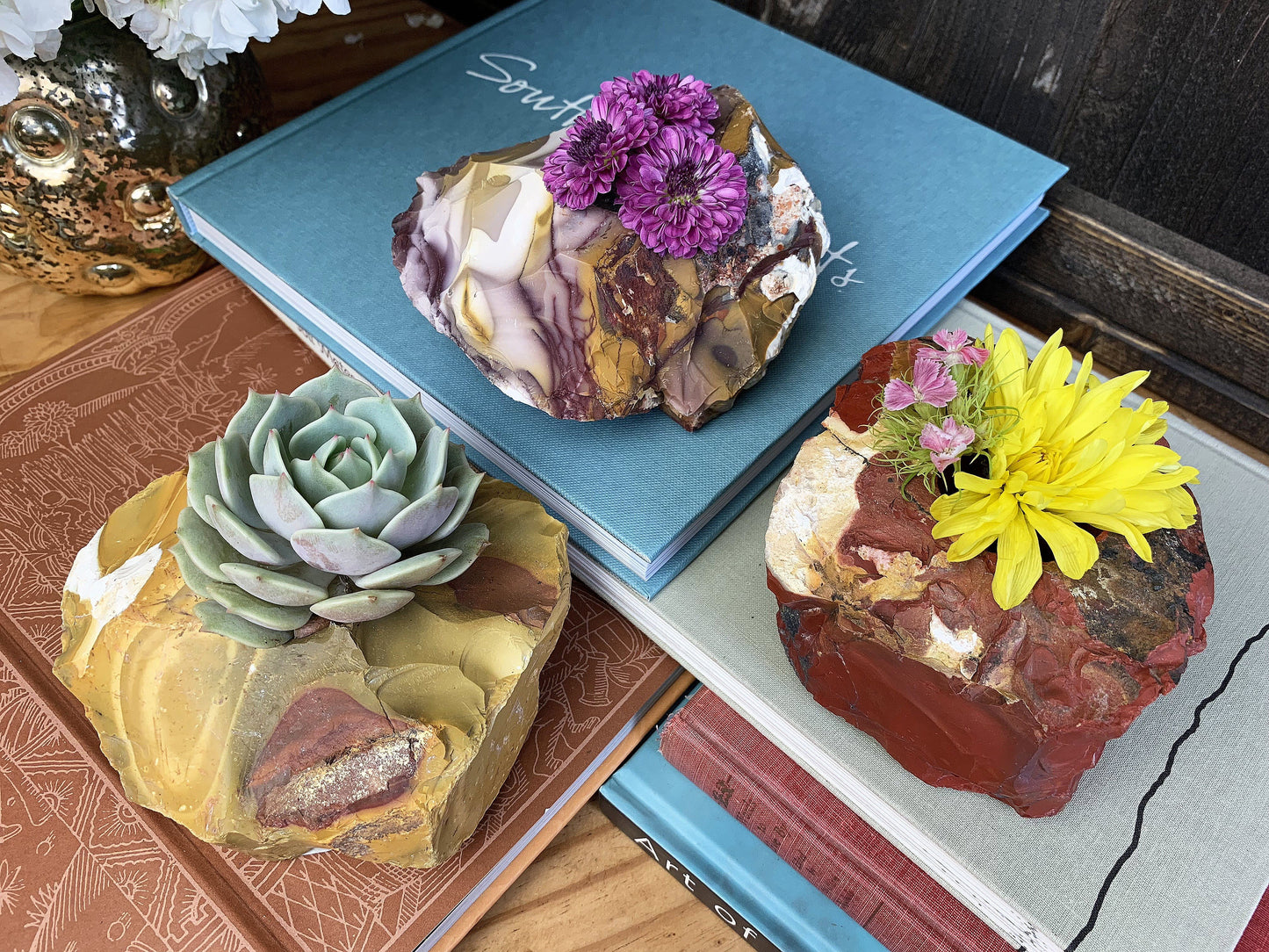 3 mookaite candle holders with flowers sticking out the top of them sitting on a multitude of books