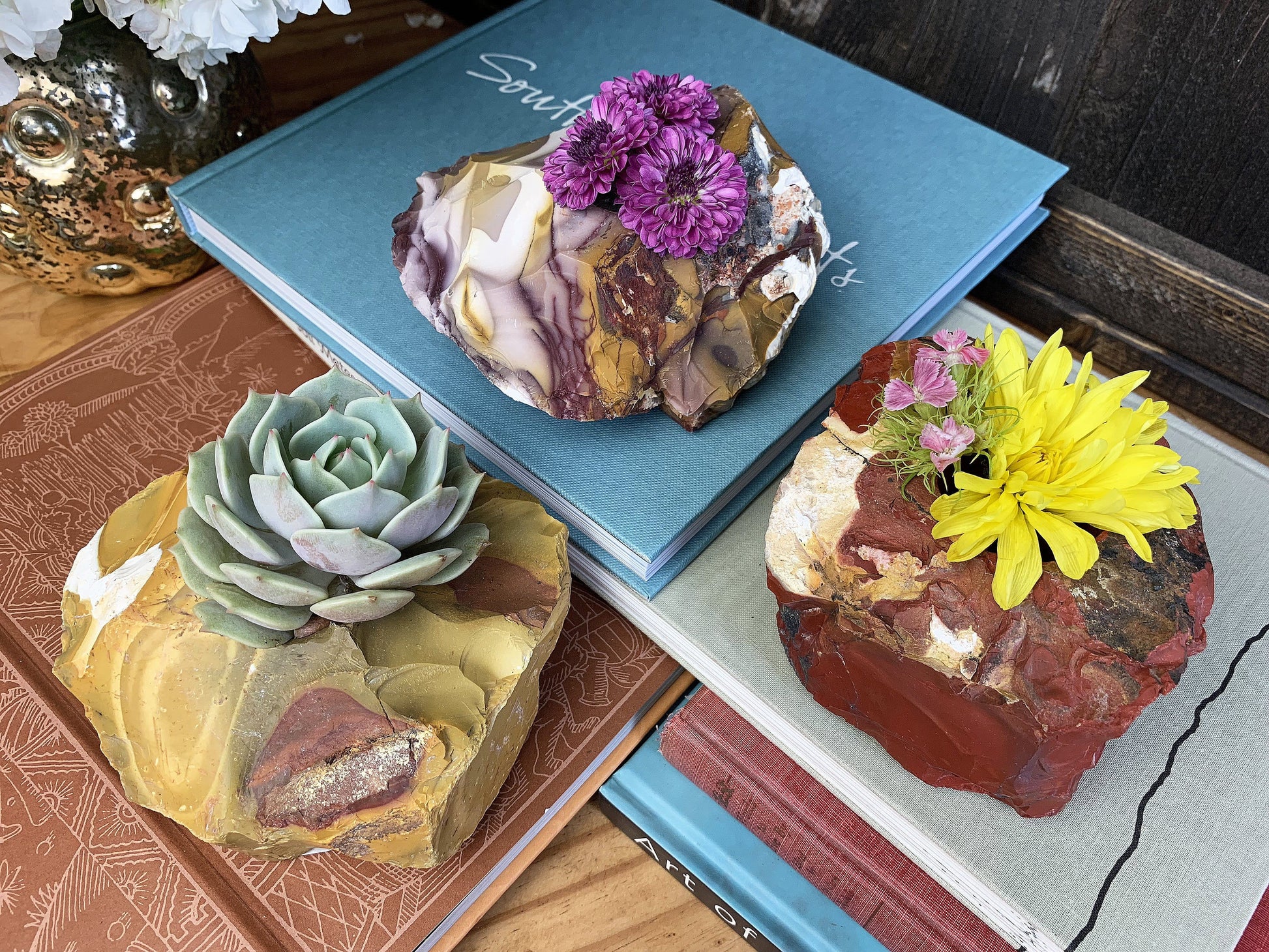 3 mookaite candle holders with flowers sticking out the top of them sitting on a multitude of books