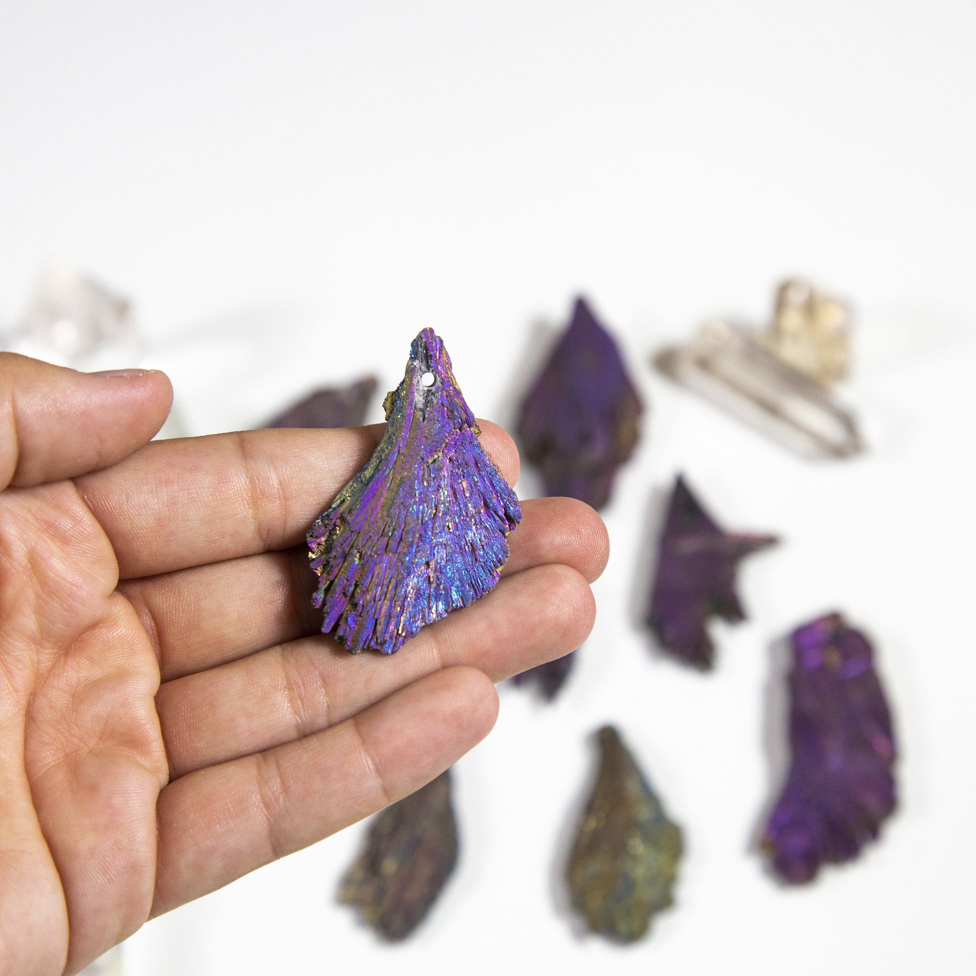hand holding up rainbow titanium treated kyanite blade with others blurred in the background