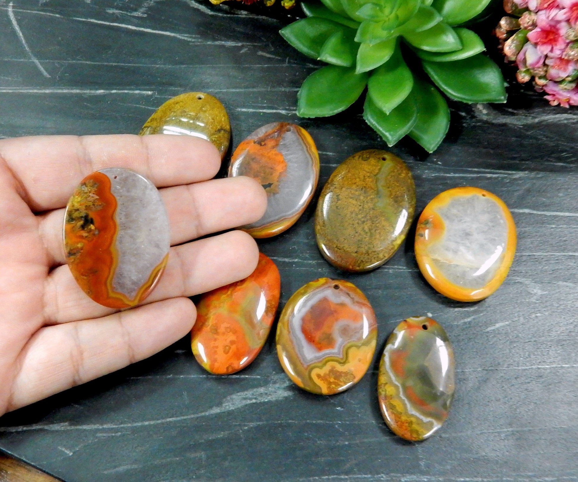 Hand holding up Red Chinese Agate Oval Shaped Bead with others on black background