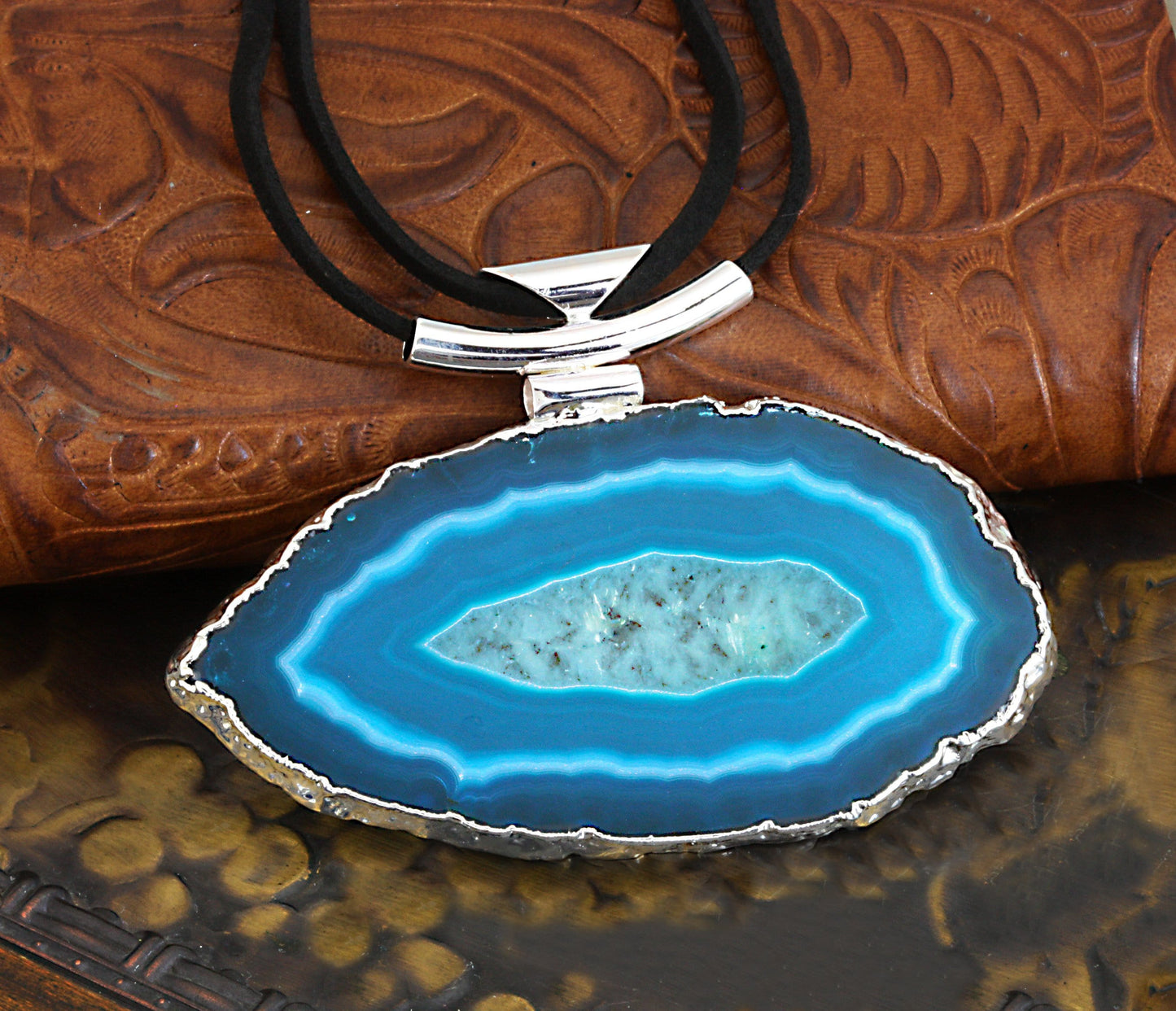 Close up of a teal agate necklace with black leather cord and a silver bail on a dark colored background.
