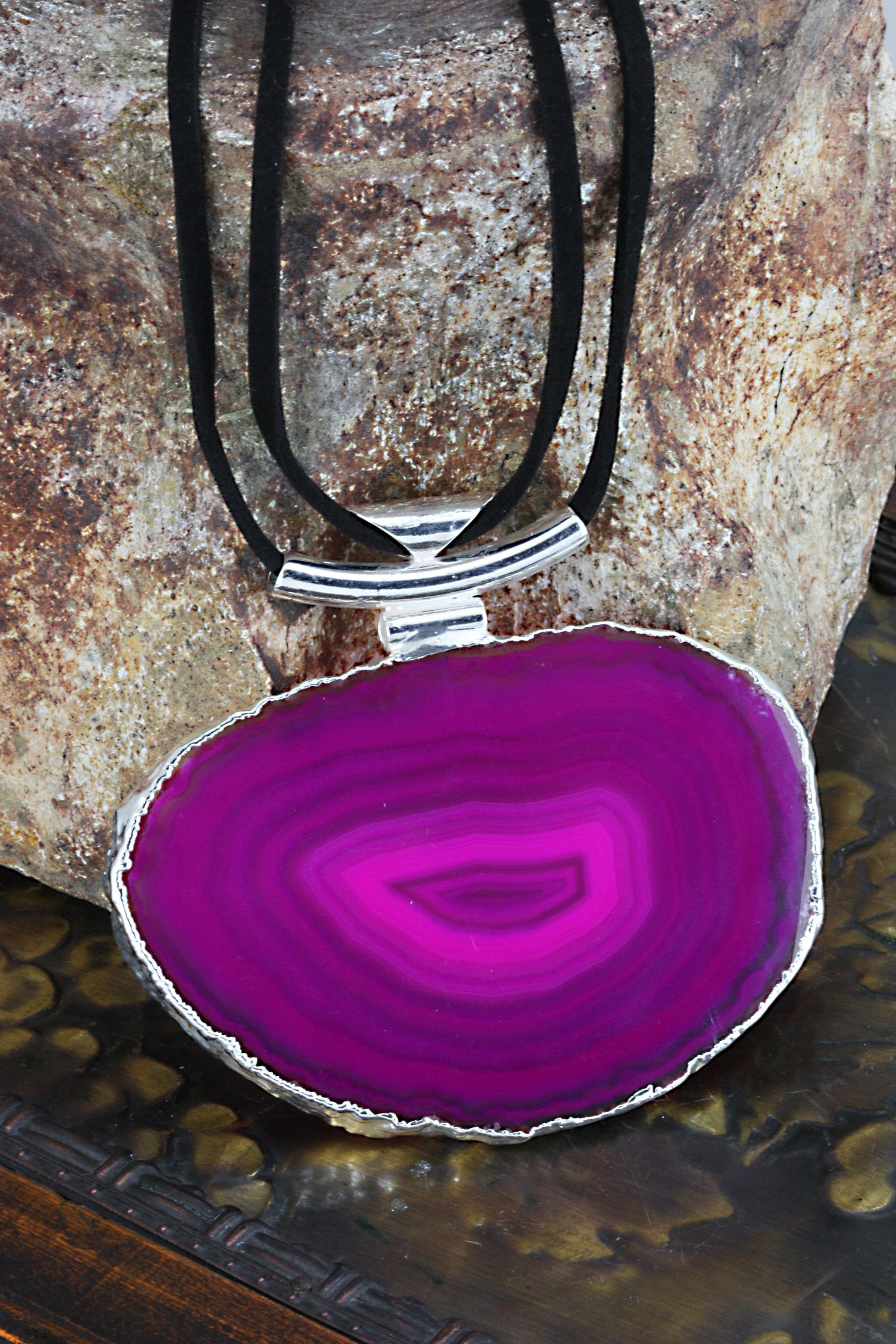 A pink agate necklace with black leather cord and silver bail on a dark colored background.