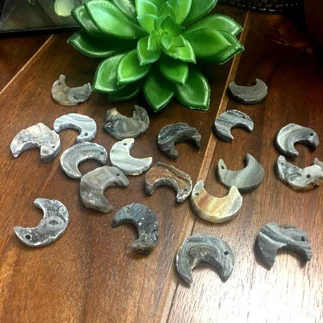 Group of Raw Chalcedony Moon Crescents scattered on wooden table with plant in the background