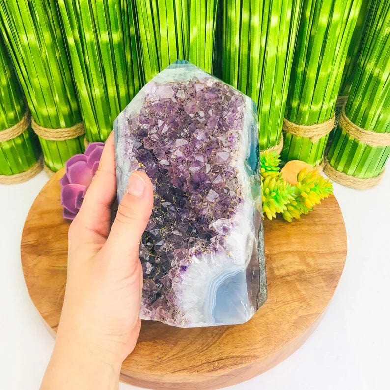 Amethyst cluster cut base with colorful agate banding in white, gray, green, and brown.  it is held in a woman's hand.