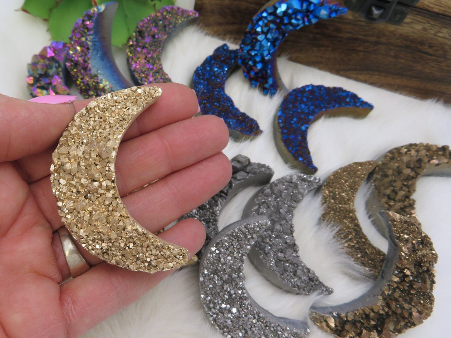 gold Titanium Druzy Stone Moon in a hand for size reference, with the mystic blue and platinum, rainbow, and bronze behind