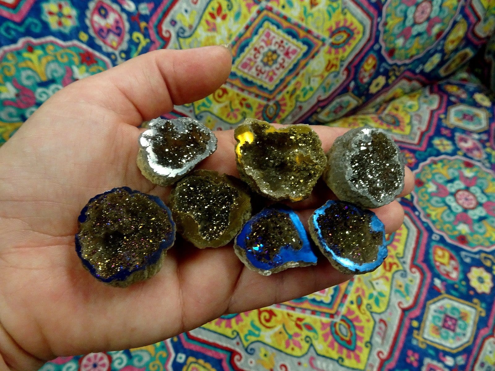 hand holding up 7 mystic half geodes in gold, platinum, and rainbow