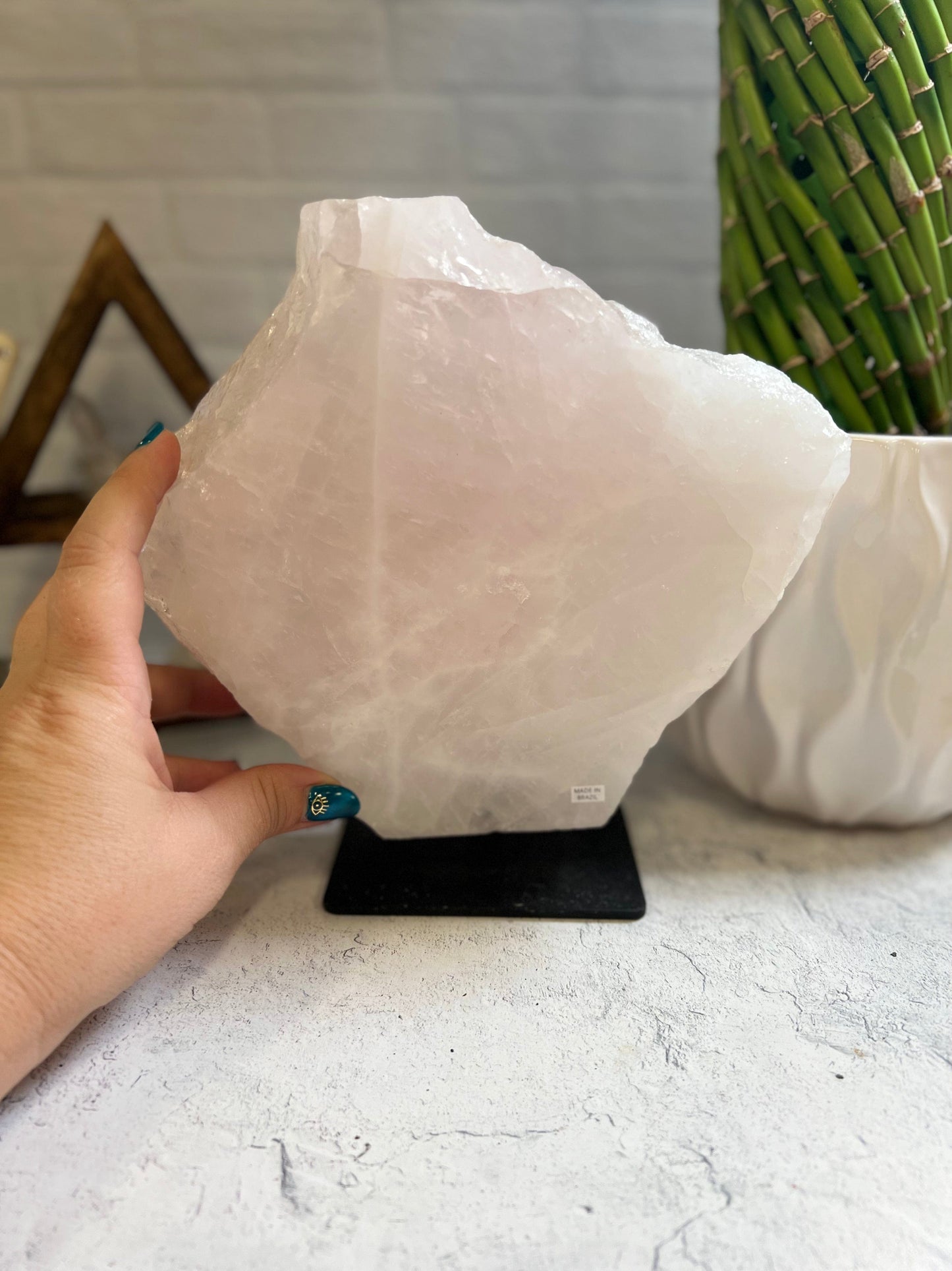 Rose Quartz large slab on a black metal base with a woman's hand next to it.