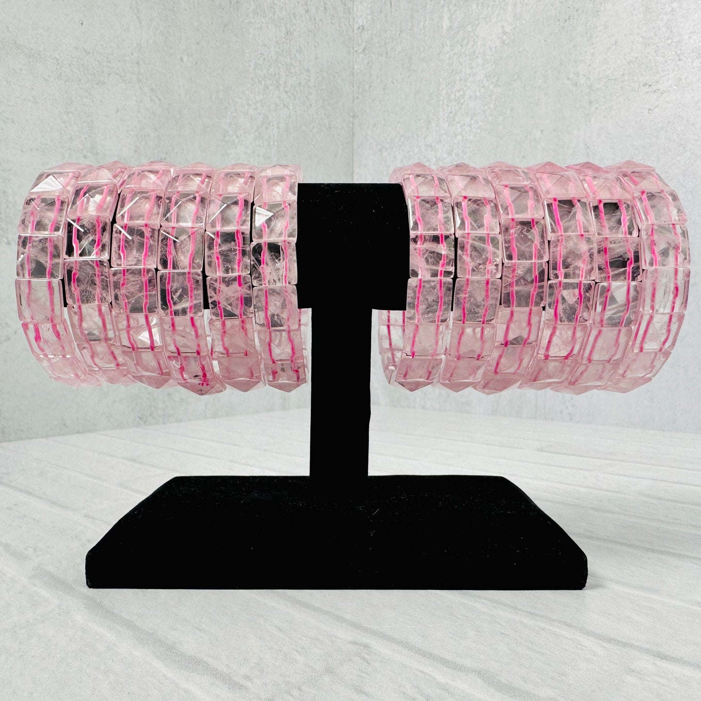 12 Rose Quartz Square Bead Bracelets on a black bracelet display.