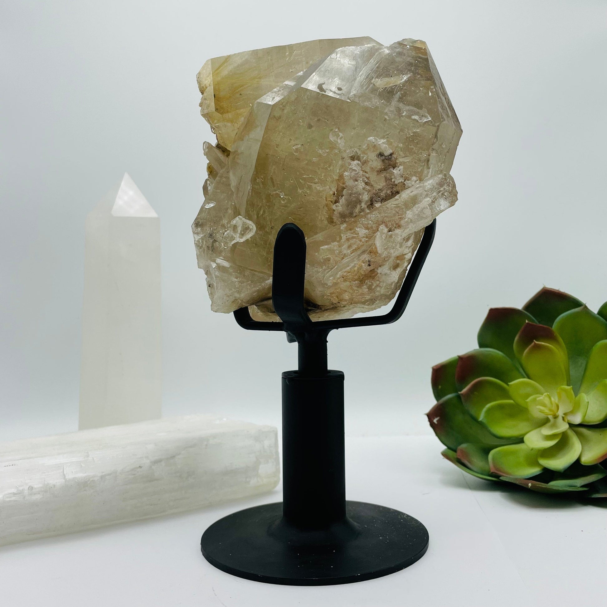 side view of Rutilated Crystal Quartz Cluster on Metal Stand with decorations in the background