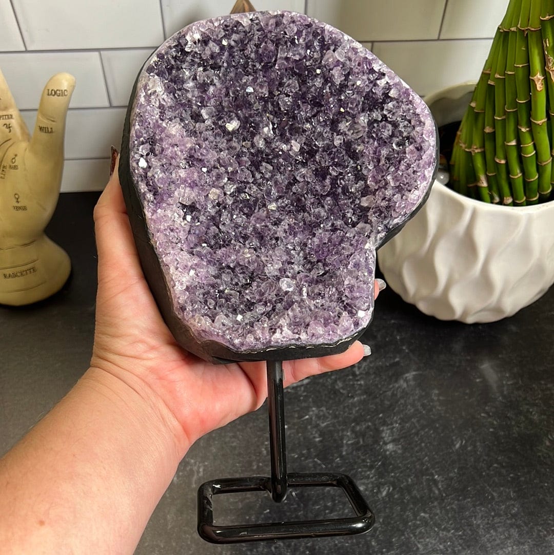 Dark purple amethyst cluster on a black metal stand held up in a woman's hand.