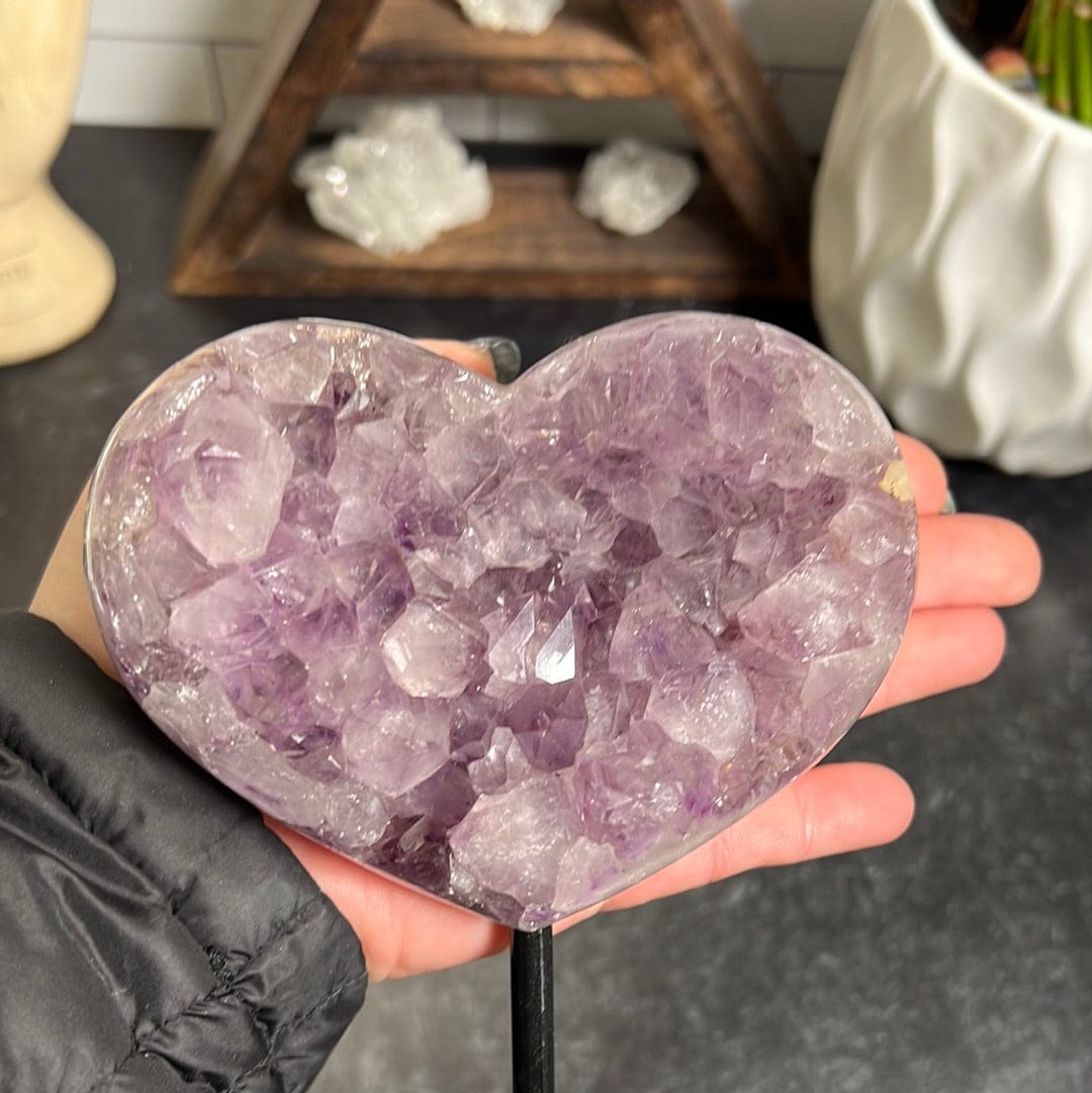 amethyst heart on a black metal stand on a black background in a woman's hand.
