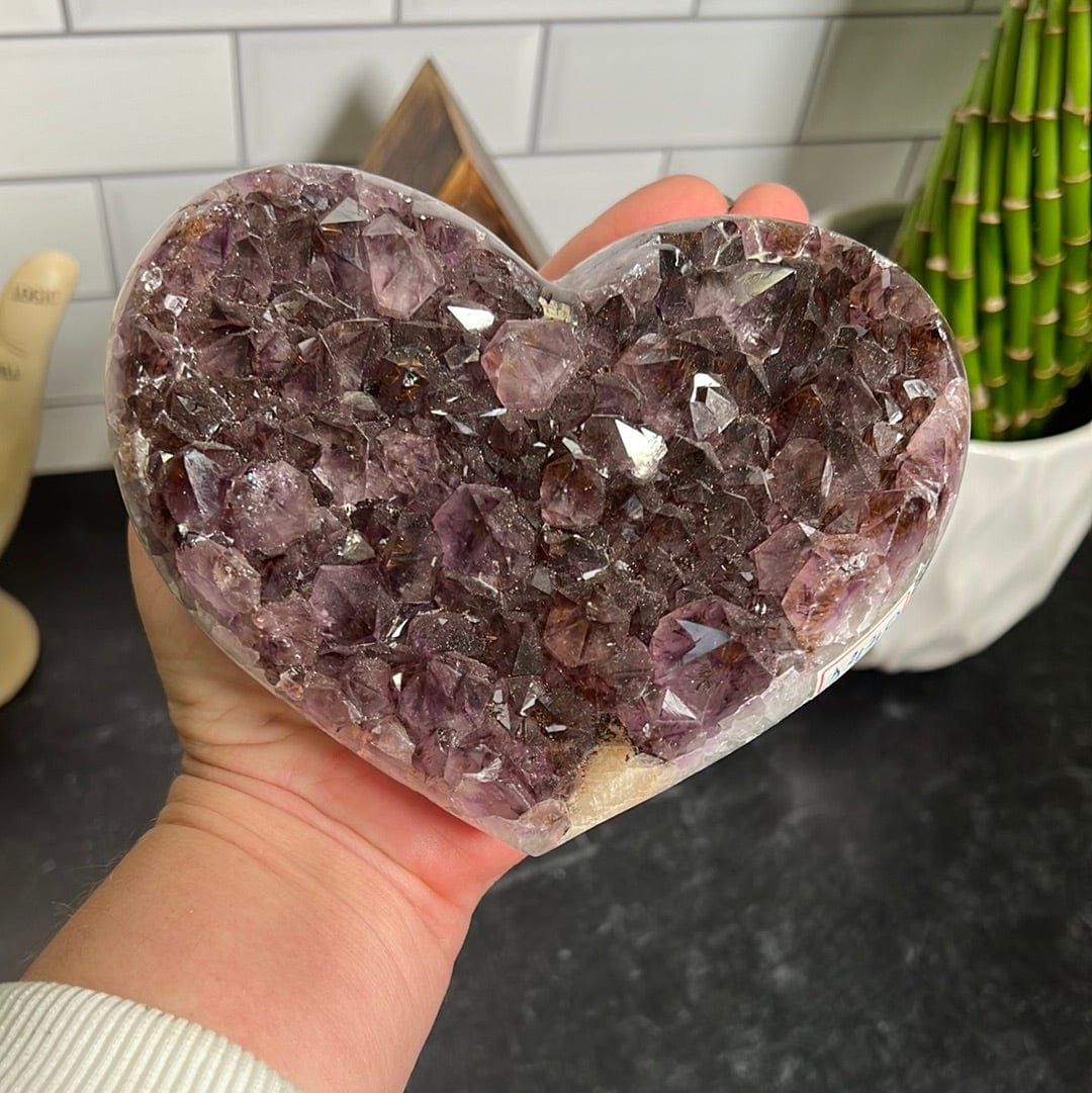 Amethyst cluster heart held in a woman's hand.