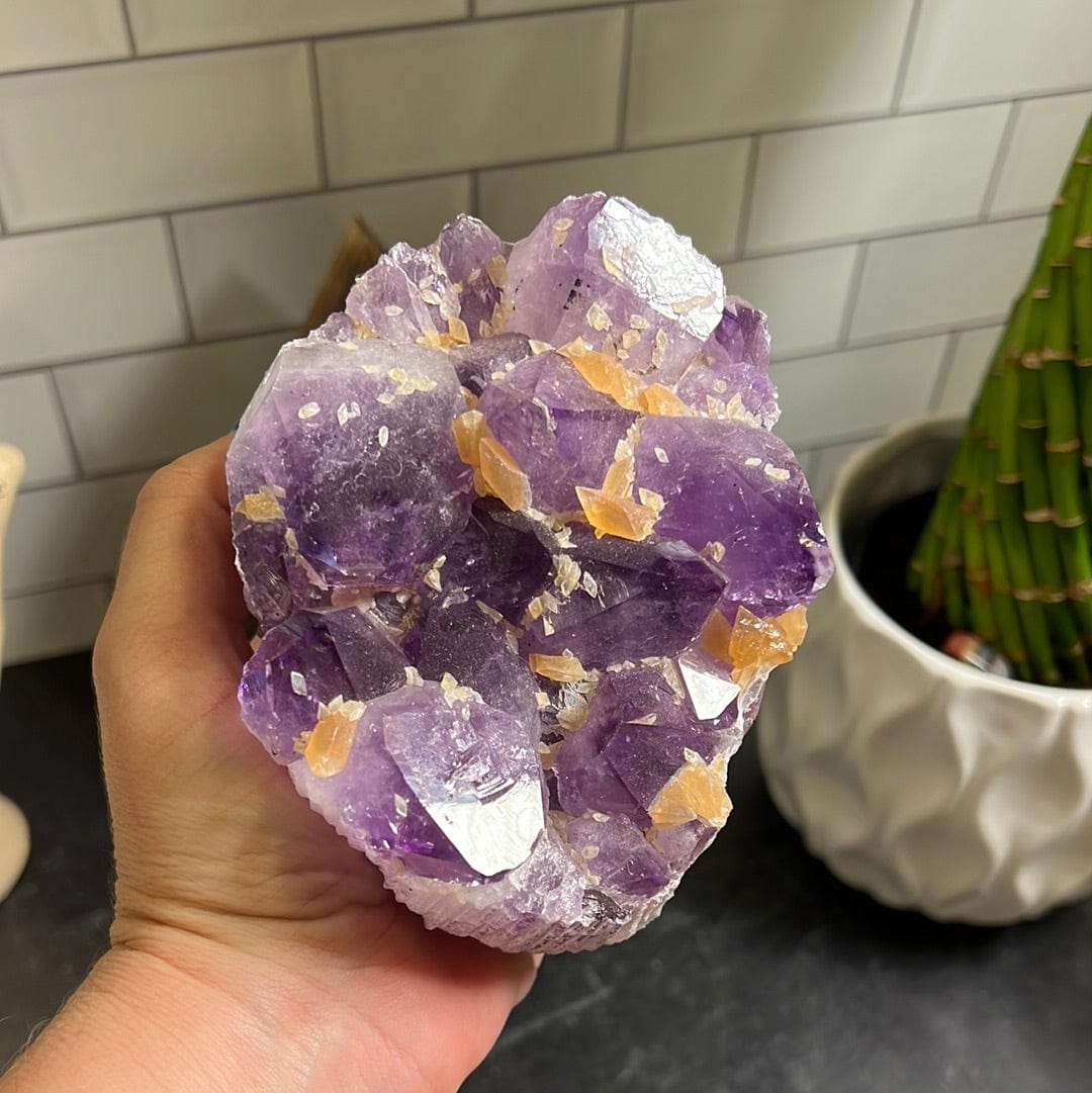 Amethyst cluster with orange calcite speckled throughout held in a woman's hand.