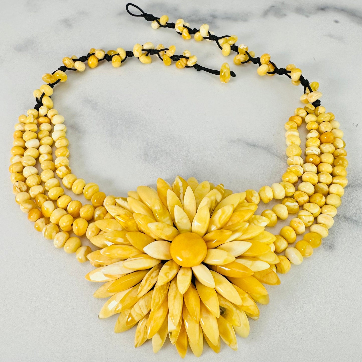 Frontal view of Yellow Baltic Amber Beaded Flower Necklace shown on a marble surface with closure undone.