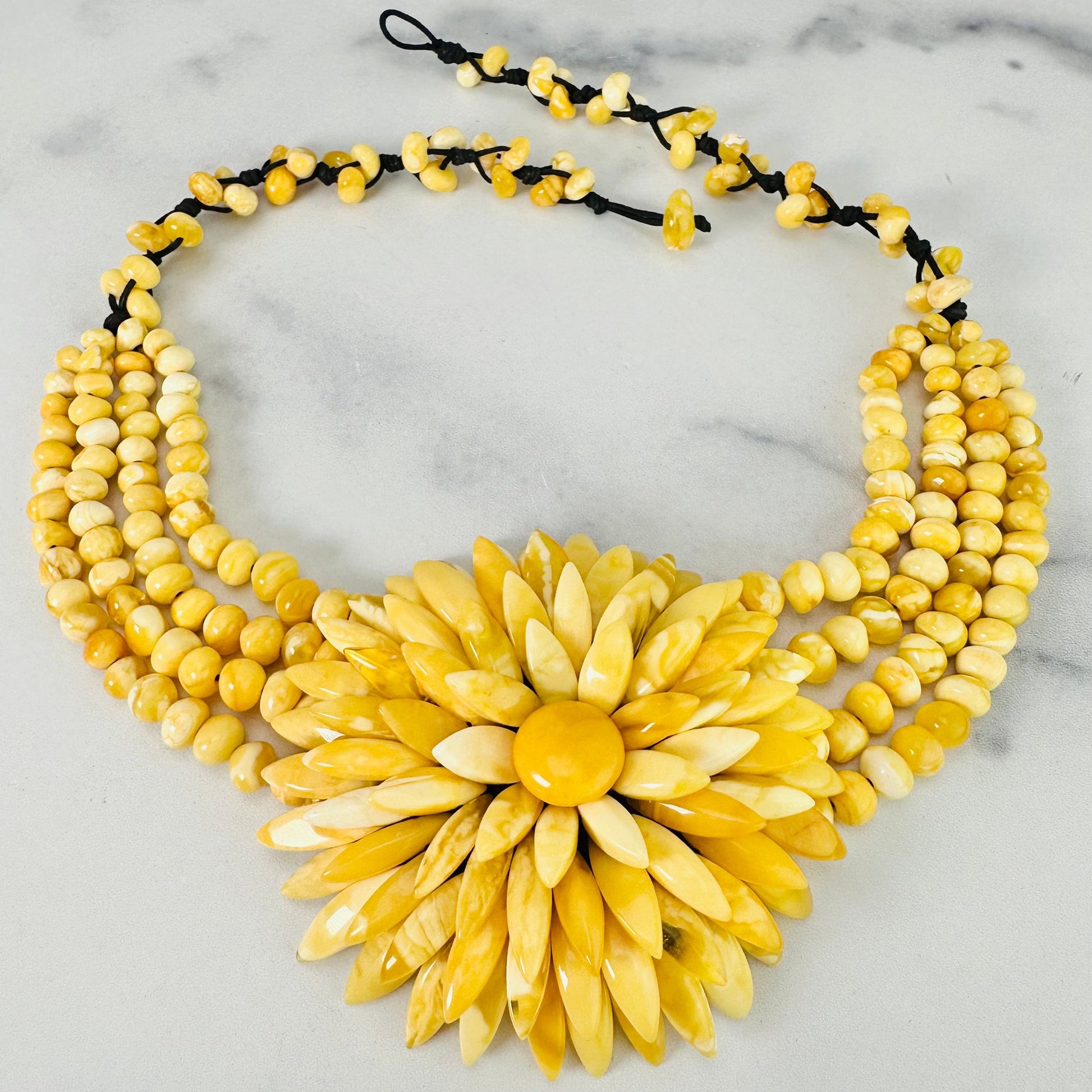 Frontal view of Yellow Baltic Amber Beaded Flower Necklace shown on a marble surface with closure undone.