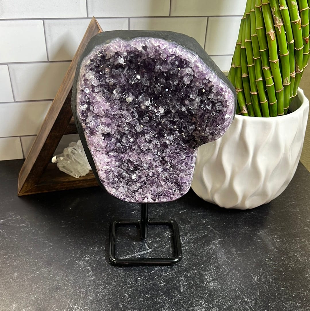 Dark purple amethyst cluster on a black metal stand on a black background.