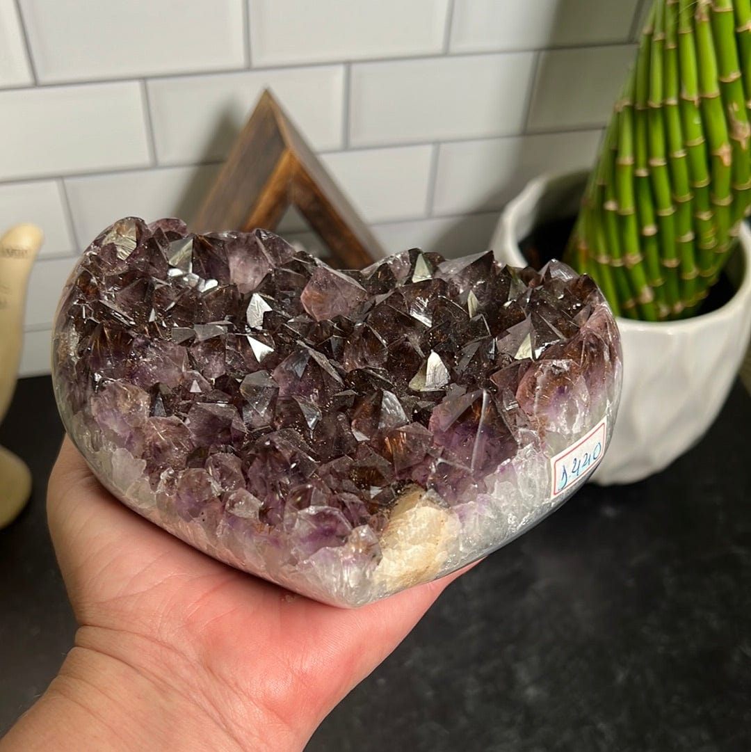 Amethyst cluster heart held in a woman's hand.  Side view showing it has white crystal on the edges