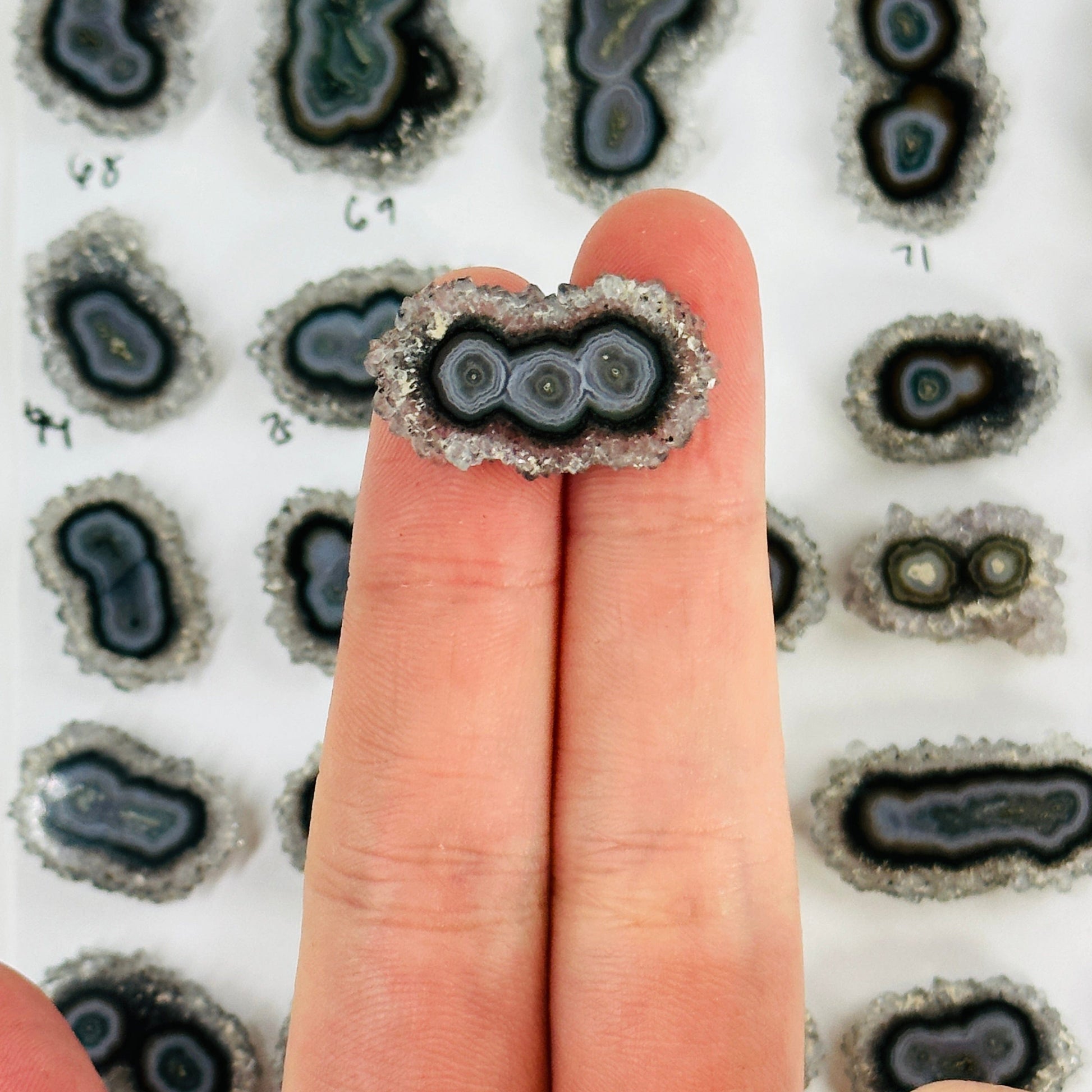 2 fingers holding up amethyst stalactite with others in the background