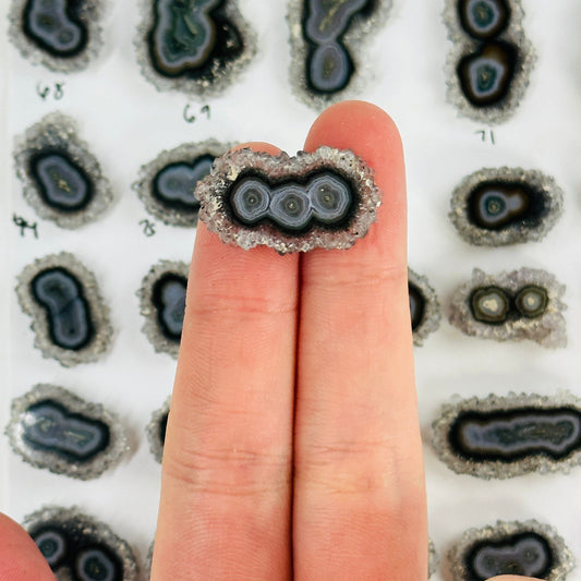 2 fingers holding up amethyst stalactite with others in the background