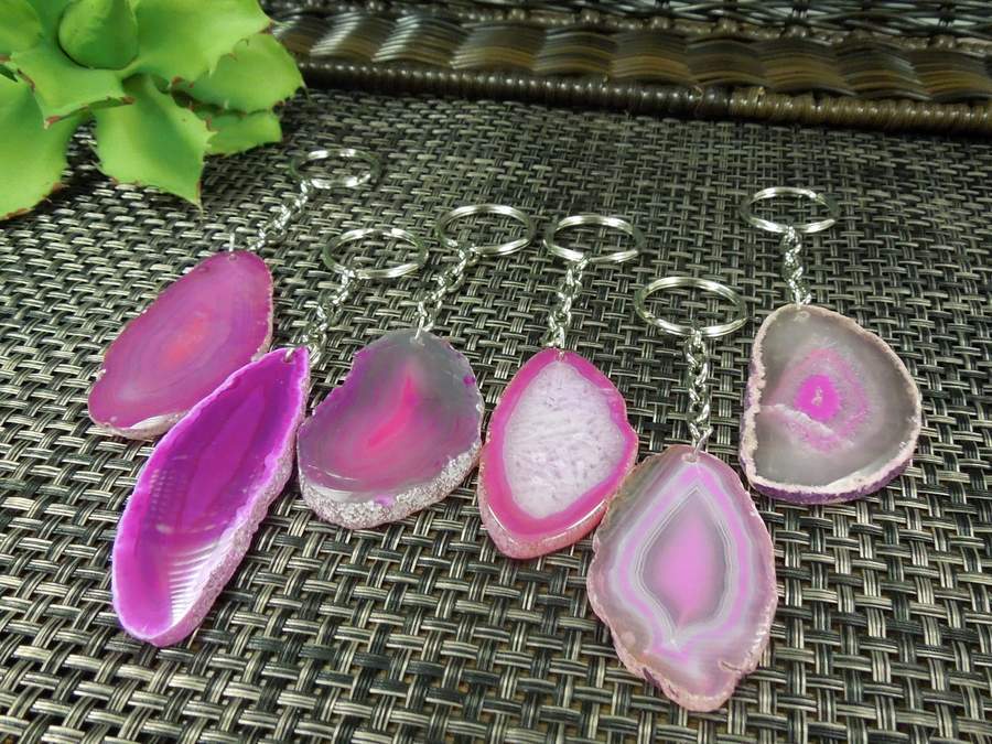 Pink agate keychains shown at an angle to display agate thickness. Agates are on a dark colored background.