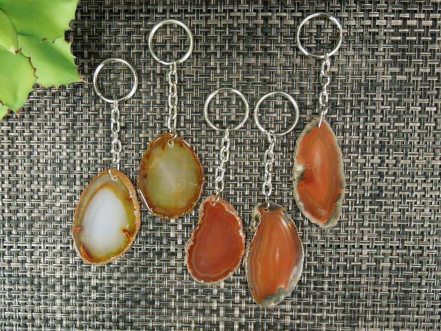 Multiple red agate keychains on a dark colored background displaying pattern, color and shape variation.
