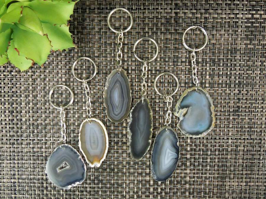 Multiple natural agate keychains on a dark colored background displaying variation in pattern, color and shape.