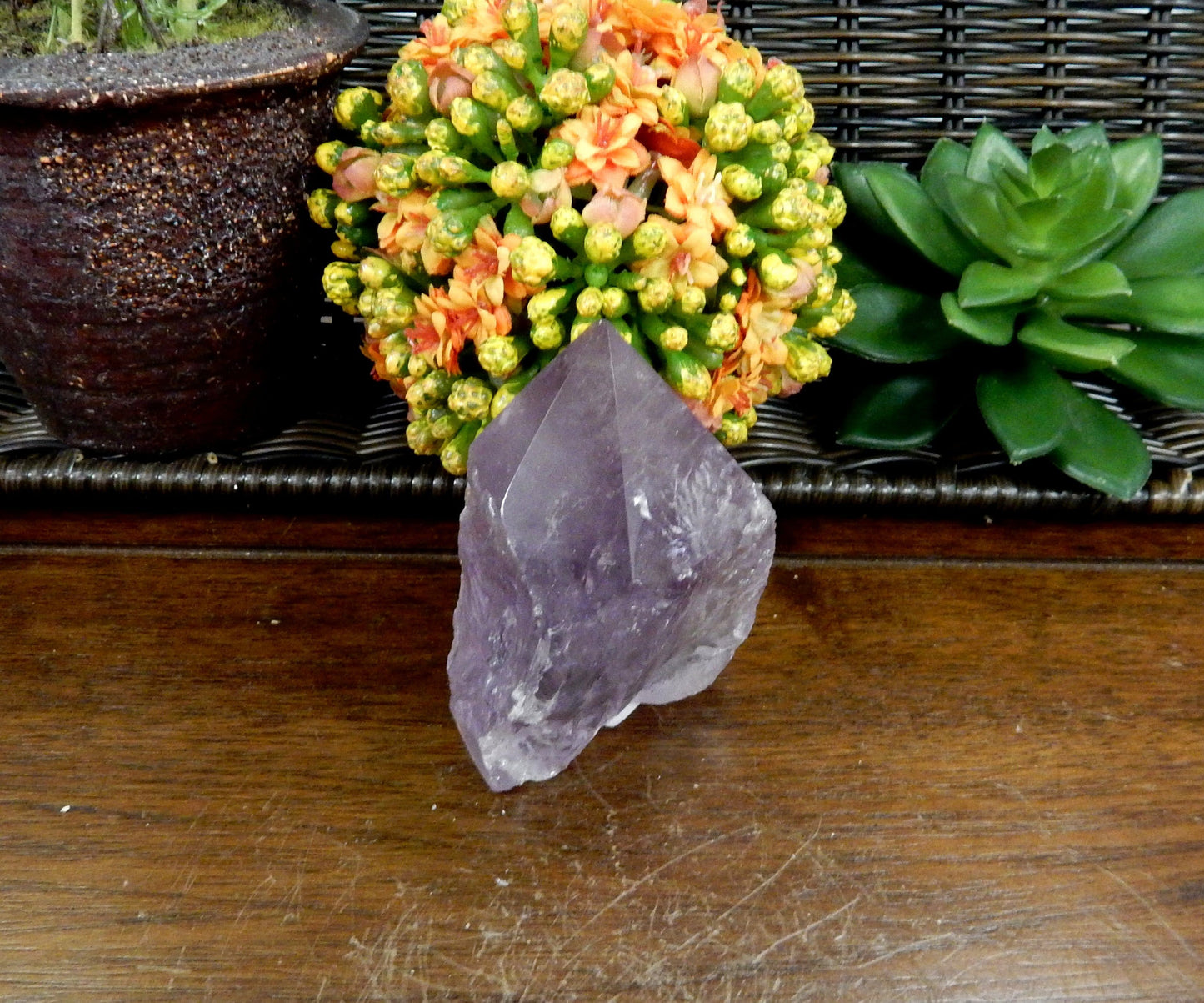 1 Raw Amethyst Semi Polished Point on wooden table with various decorations in the background