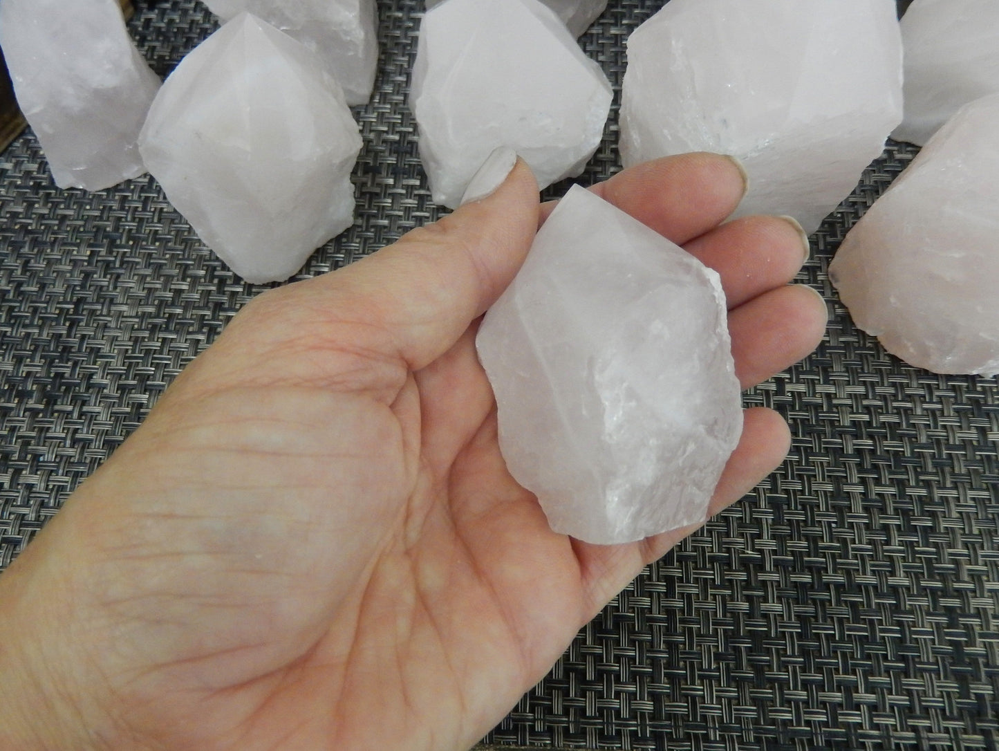 Hand holding up Rose Quartz Semi Polished Point with others behind it