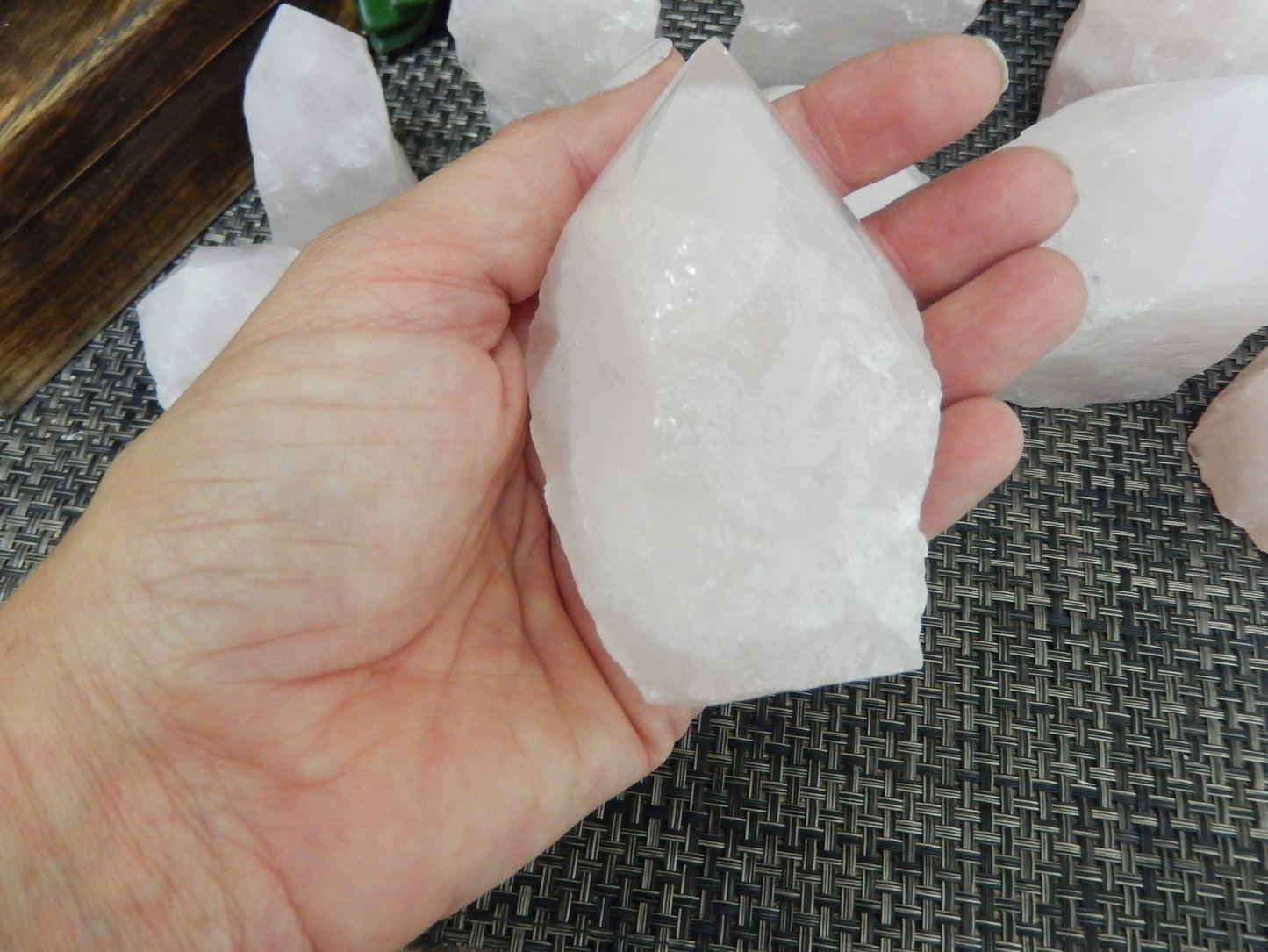 Hand holding up Rose Quartz Semi Polished Point with others behind it