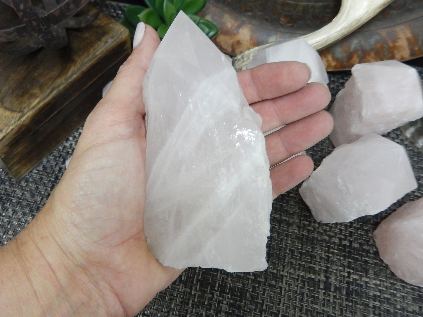 Hand holding up Rose Quartz Semi Polished Point with others behind it