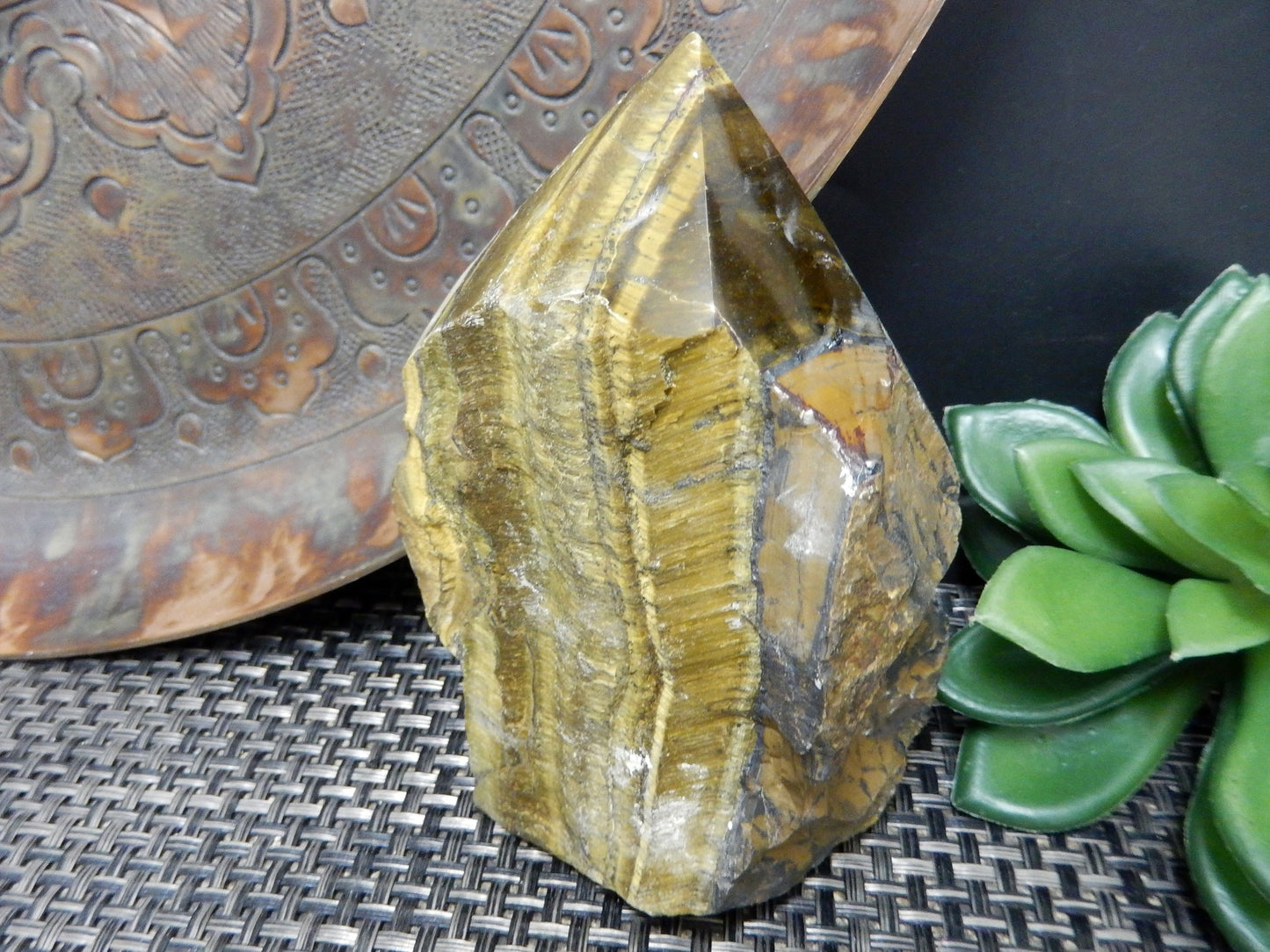 Tiger eye point with a polished top and rough base on a brown background.
