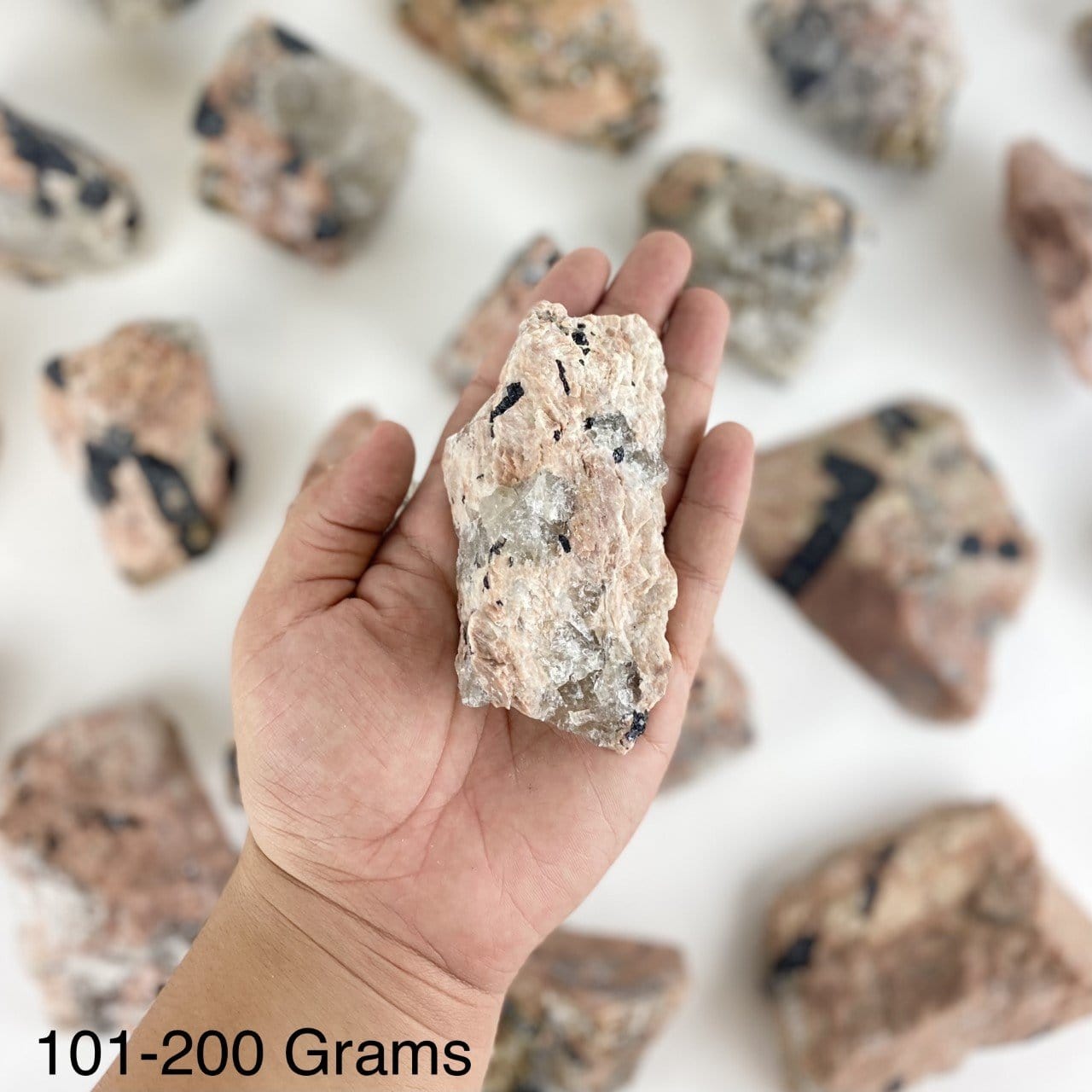 One piece of Feldspar with Black Tourmaline in the hand showing the weight of 101-200 grams.