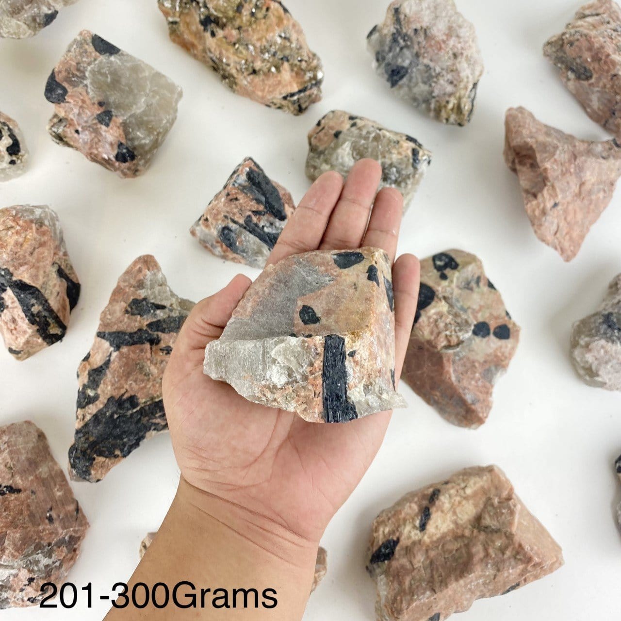 One piece of Feldspar with Black Tourmaline in the hand showing the weight of 201-300grams.